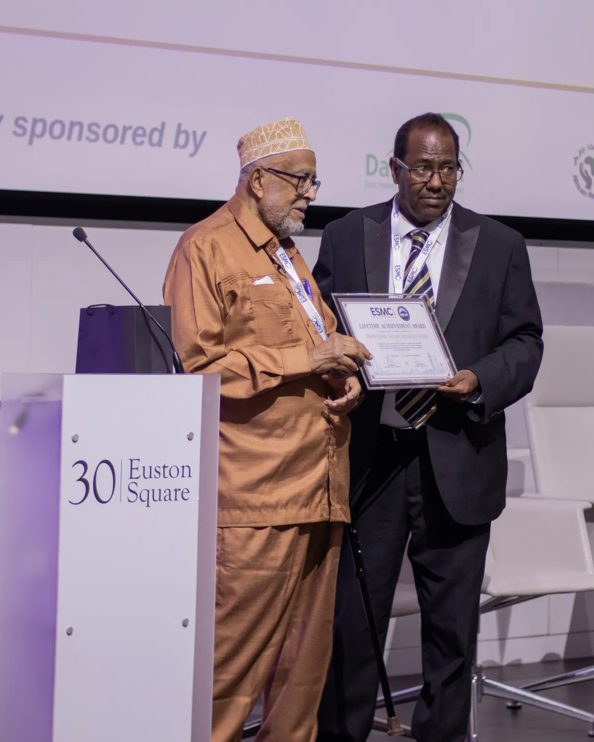 Professor Salah Aidarous Nasir holds his ESMC 2026 Lifetime Achievement Award certificate on stage at 30 Euston Square